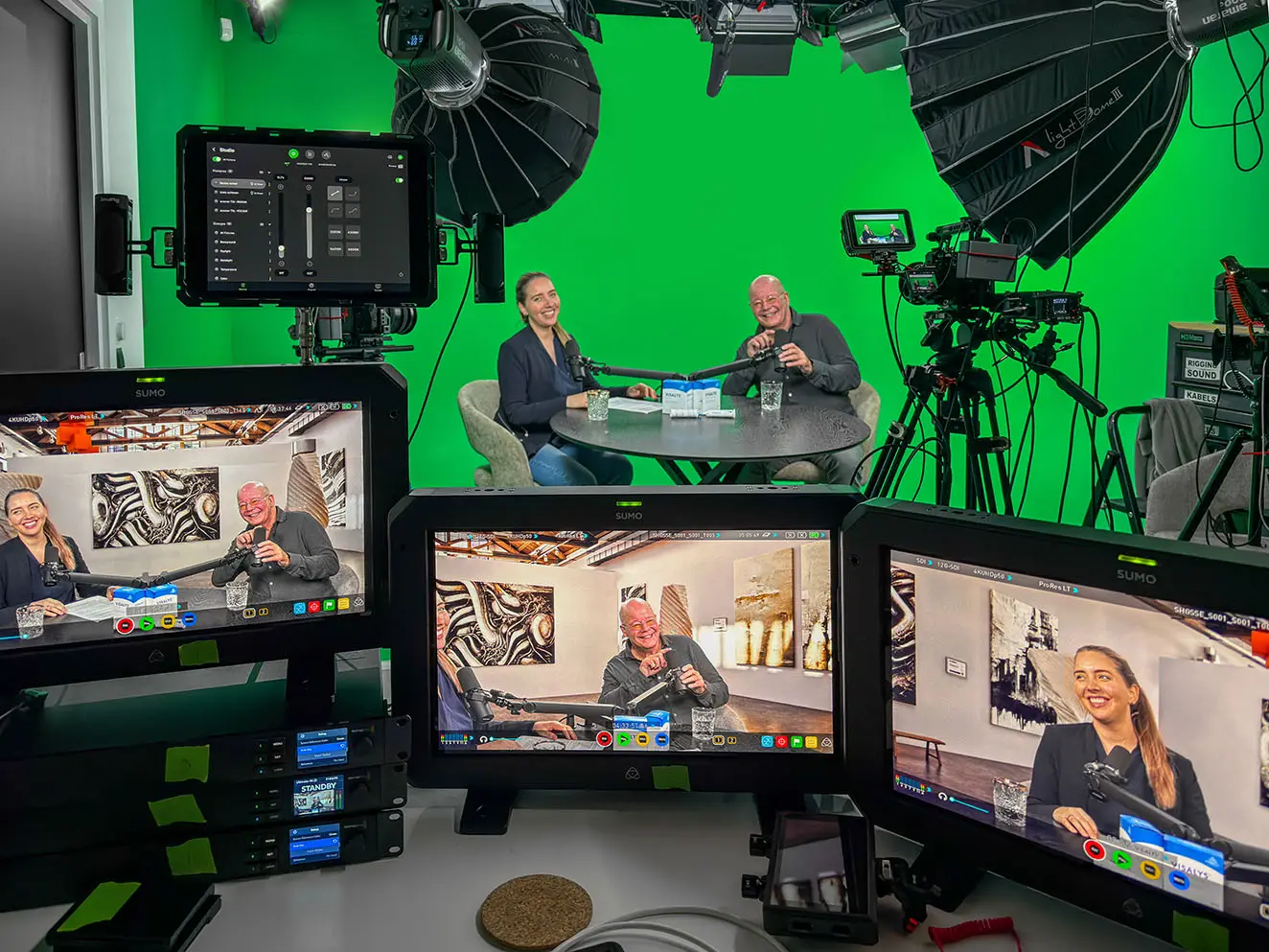 Twee podcastgasten voor het green screen in Breda, met op de regiemonitoren het eindresultaat in een virtuele loftset.